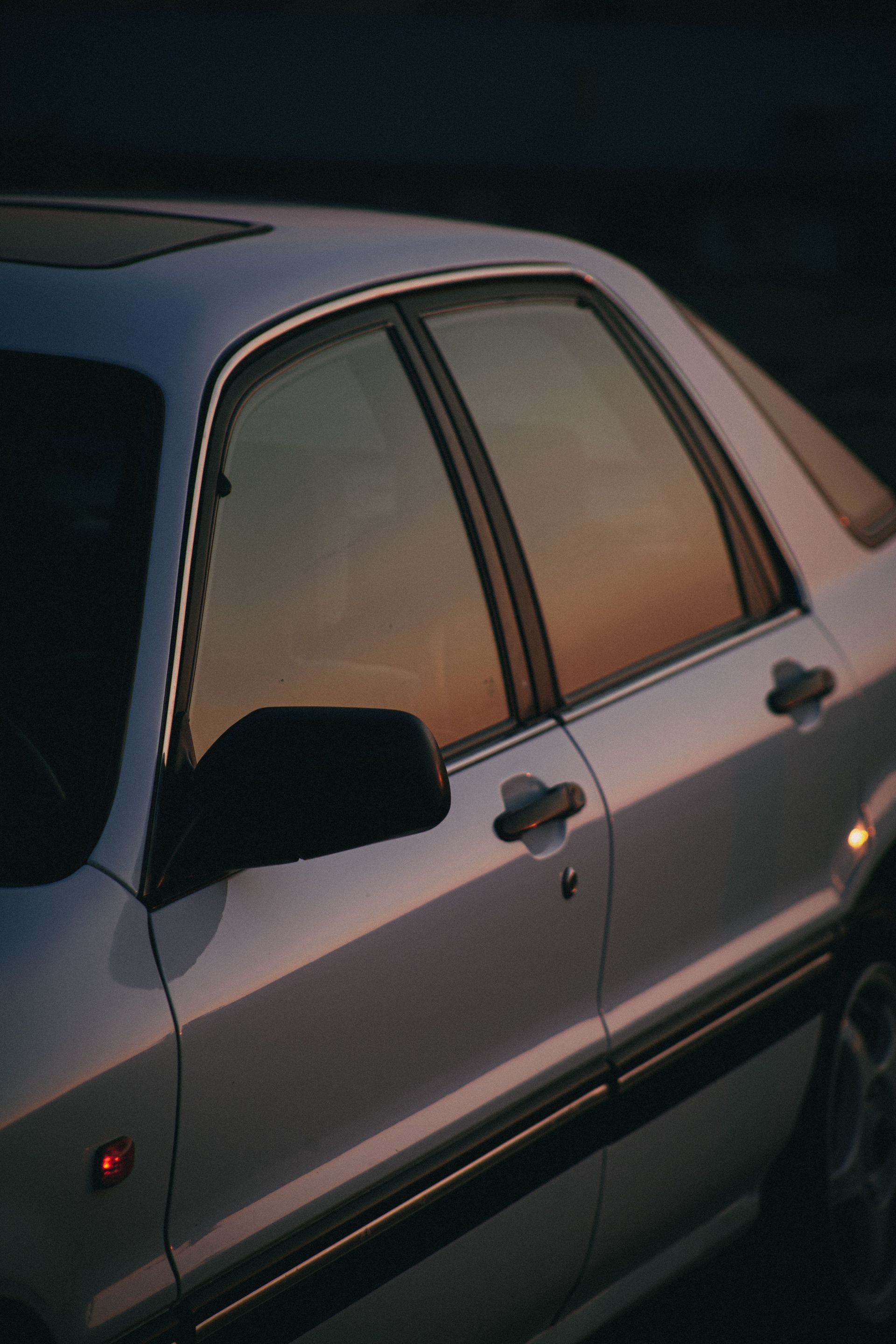 Silver car with sunset reflection on window, exuding elegance and serenity.
